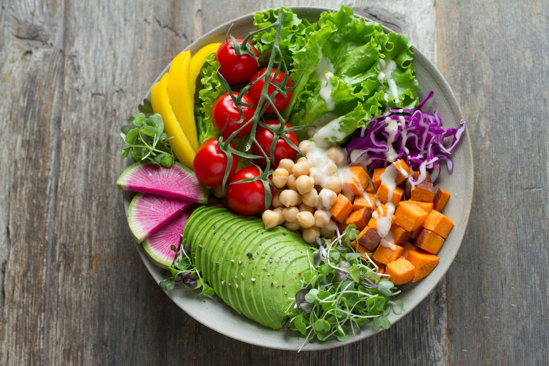 A colourful bowl of vegetables with avocado, chickpeas, tomatoes and leafy greens on a wooden table.