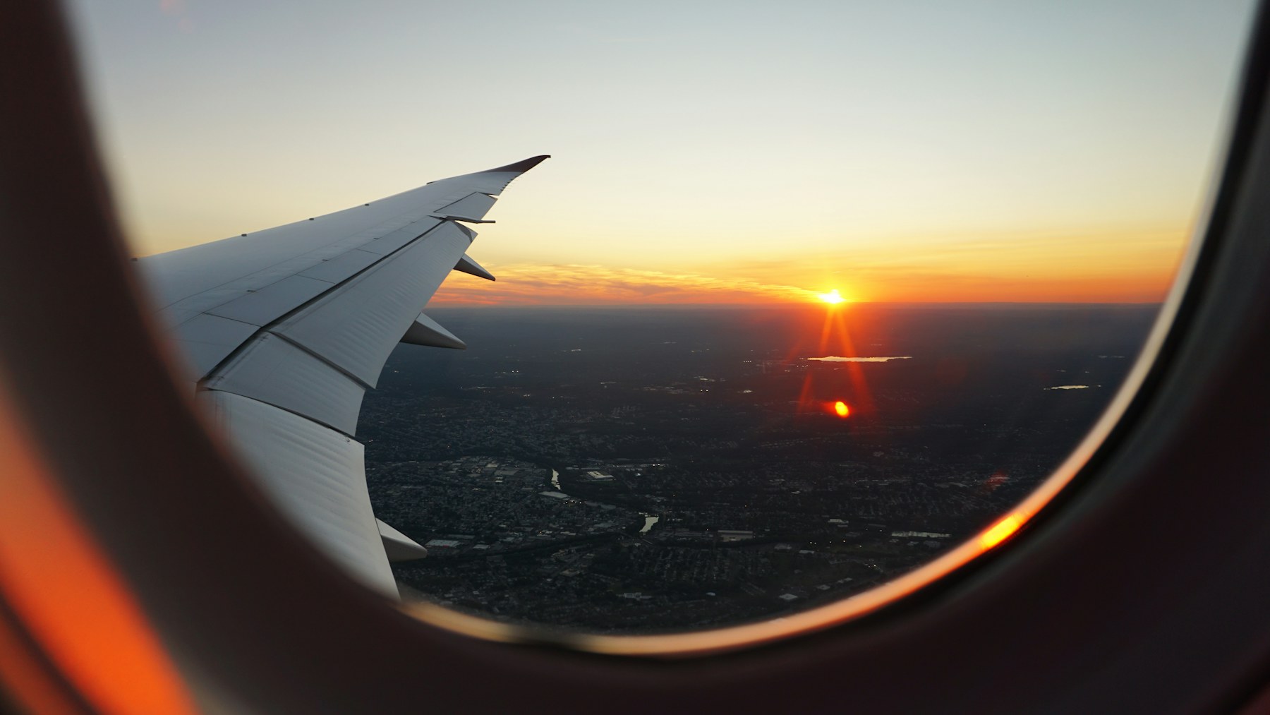 An aircraft wing and a sunset seen through a passenger window.