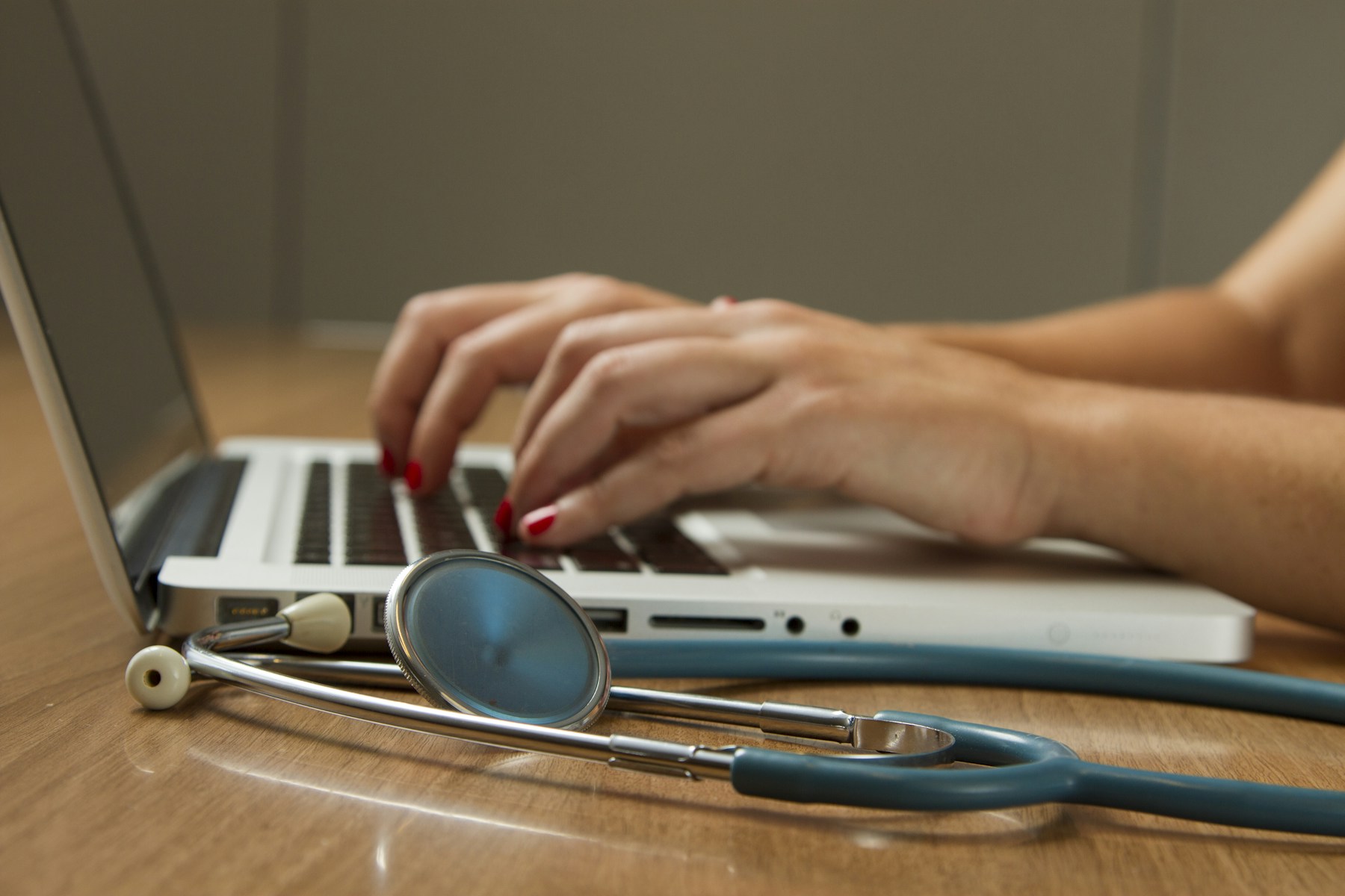 A stethoscope beside a laptop as a healthcare professional works on medical documentation.