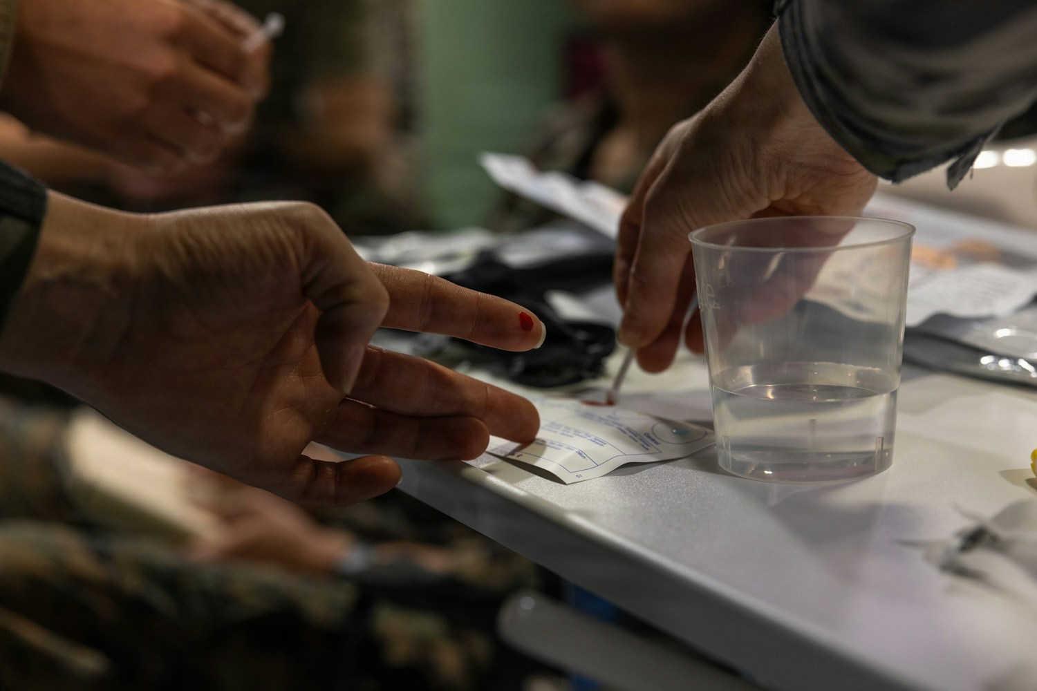 A small drop of blood on a fingertip beside a medical test card.