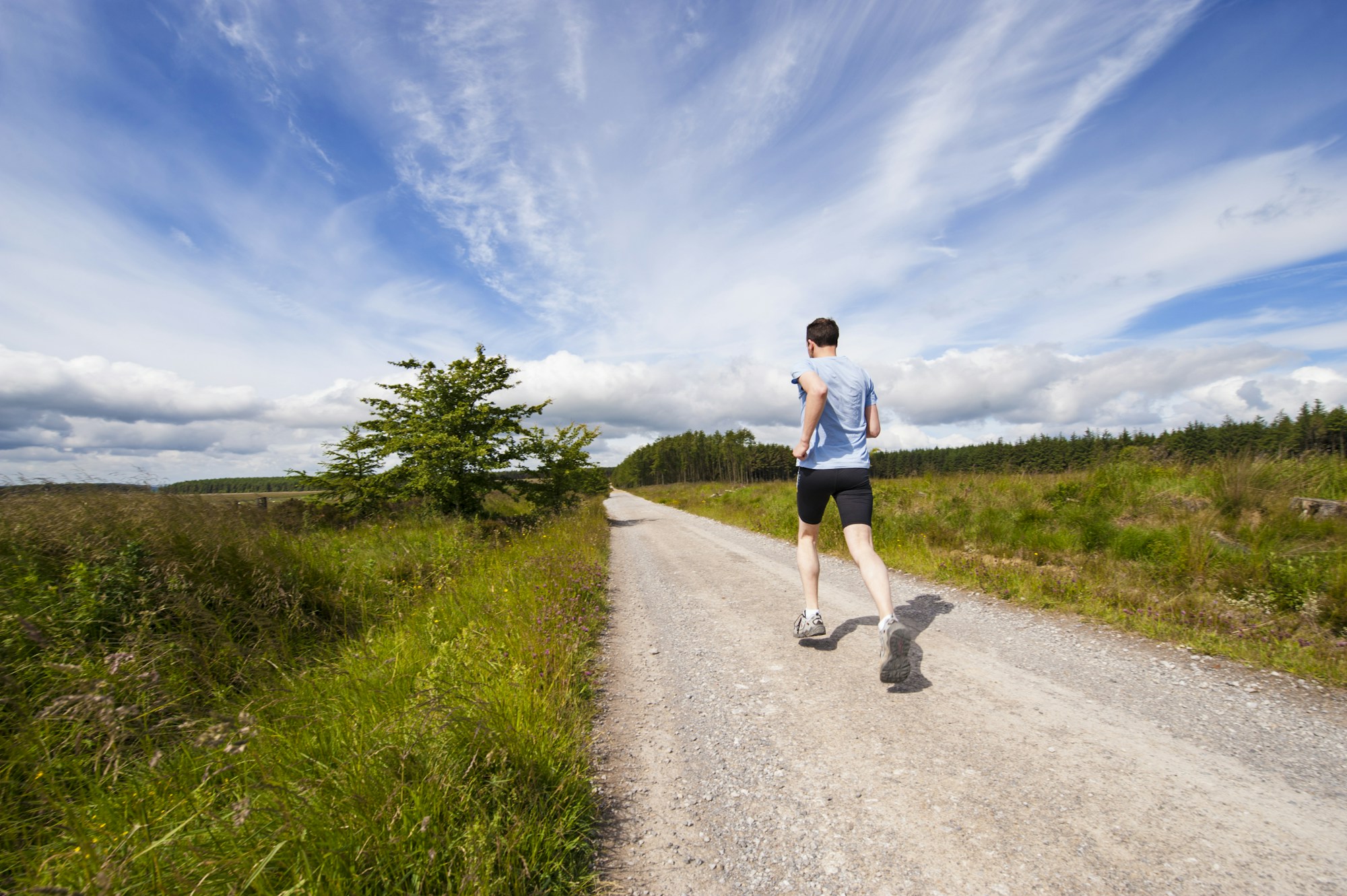 An athlete running along a country road beside green fields.